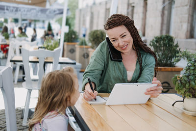 Busy successful mother and business owner with cell phone and tablet having breakfast with her