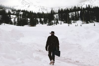 Rear view of man walking on snow covered landscape
