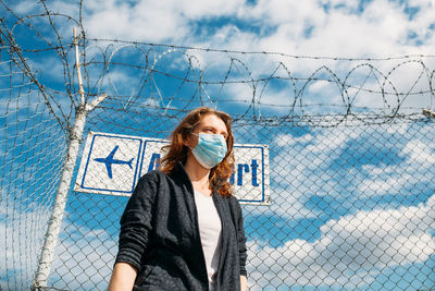 Portrait of woman standing by chainlink fence against sky