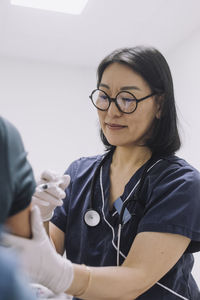 Female doctor wearing eyeglasses injecting patient in hospital