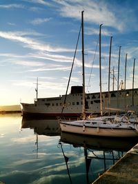 Sailboats moored in harbor at sunset