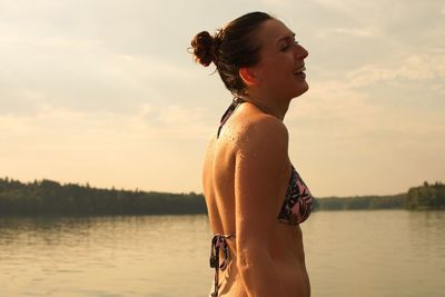 Side view of woman in bikini top standing by lake