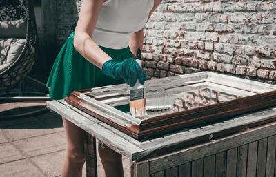 A young girl paints a mirror frame.