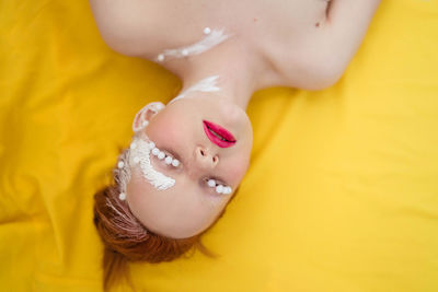 Portrait of a young woman in white art makeup on a yellow background