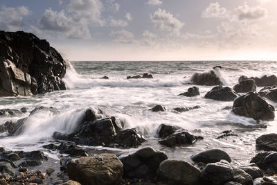 Waves splashing on rocks in sea against sky