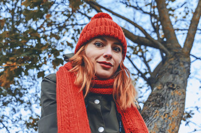 Smiling cute young woman in orange warm knitted hat and scarf. autumn portrait close-up. 