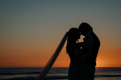 Couple standing by sea against sky during sunset