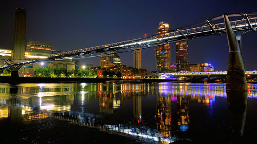 Illuminated buildings by river against sky at night