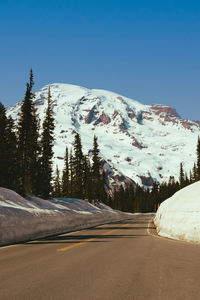 Road by snowcapped mountains against clear sky during winter