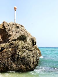 Rock formation in sea against clear sky