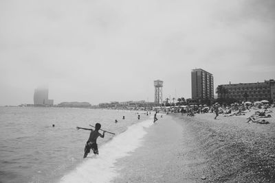 People enjoying at beach by city against sky