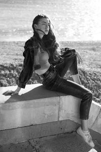 Full length of woman sitting on retaining wall against sea