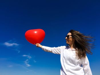 Woman holding balloon against blue sky