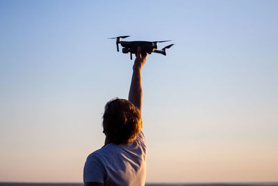 Rear view of man with arms raised against clear sky