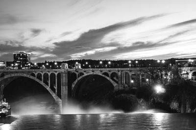 Arch bridge over river against sky in city at night