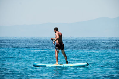 Full length of shirtless man standing in sea against sky