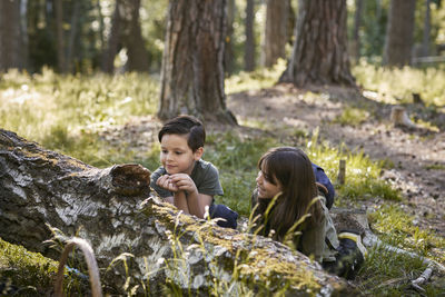 Boy and girl sitting near fallen tree in forest