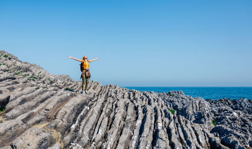 Young woman raising arms hiking through flysch rock landscape