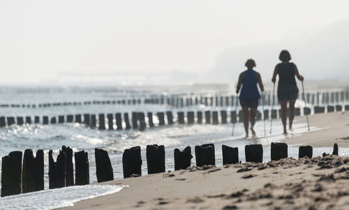 Rear view of women walking at beach against sky