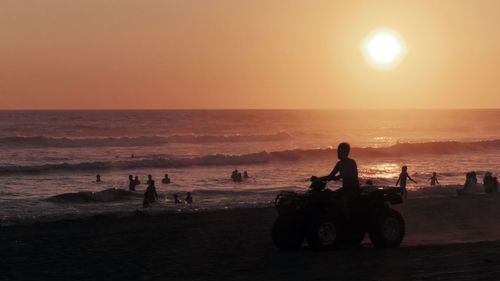 Man riding quadbike at beach against sky during sunset
