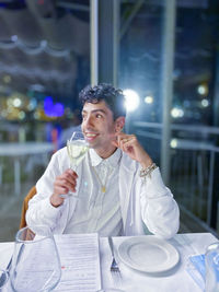 Portrait of a smiling young man drinking glass on table at restaurant