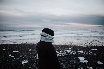 Man looking at frozen sea while standing against cloudy sky during sunset