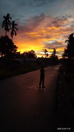 Silhouette people on road against sky during sunset