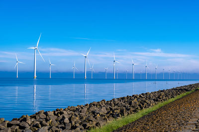 Wind turbines in sea against blue sky