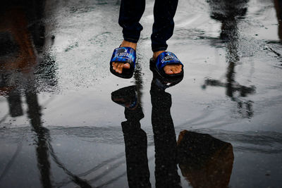 Low section of man standing on puddle during rainy season