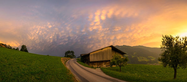 Road amidst field against sky during sunset