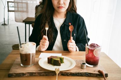 Midsection of woman holding fork and spoon while sitting on table at restaurant