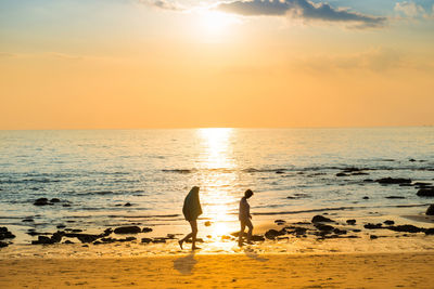 Silhouette people on beach against sky during sunset