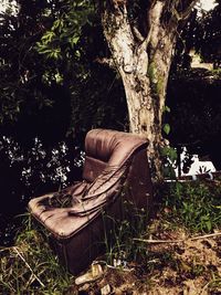 Abandoned chair on field against trees