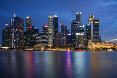 Illuminated skyscrapers by sea against sky at night