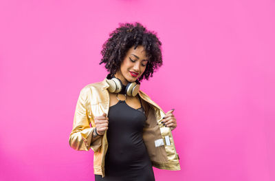 Fashionable young woman with curly hair against pink background