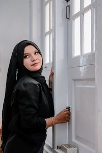 Portrait of young woman looking through window