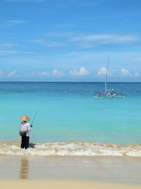 Rear view of man fishing in sea against sky during sunny day