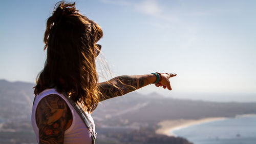 Rear view of tattooed woman pointing the horizon against sky during sunset