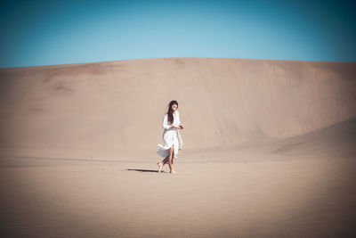 Side view of woman walking on sand dune at desert against clear sky during sunny day