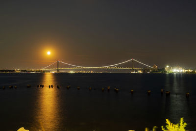 Illuminated bridge over river against sky at night