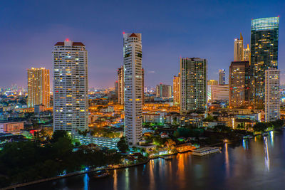 Illuminated buildings by river against sky in city at night