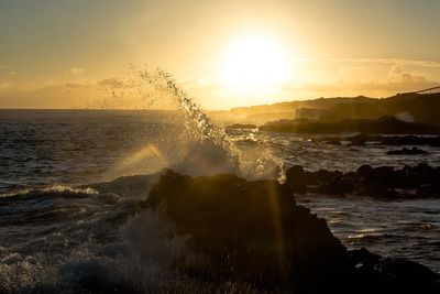 Water splashing in sea against sky during sunset