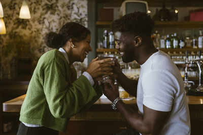 Multiracial couple toasting drinks while celebrating at bar