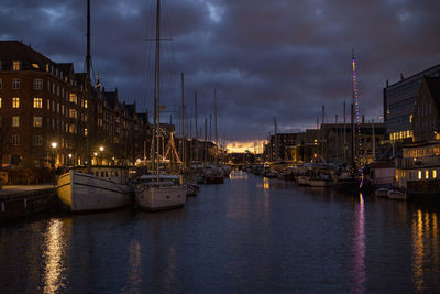 Sailboats moored on canal in city against sky at night