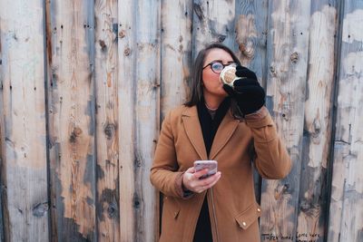 Portrait of young woman drinking while standing against wall