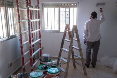 Young woman painting interior wall with white paint. paint cans and painter ladder.
