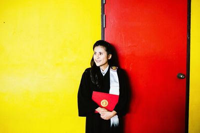 Young woman standing against red wall