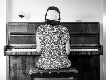 Rear view of woman playing piano at home
