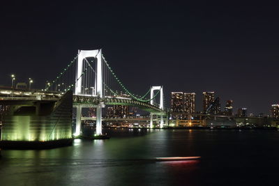 Illuminated rainbow bridge over tokyo bay in city at night