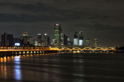 Illuminated buildings by river against sky at night